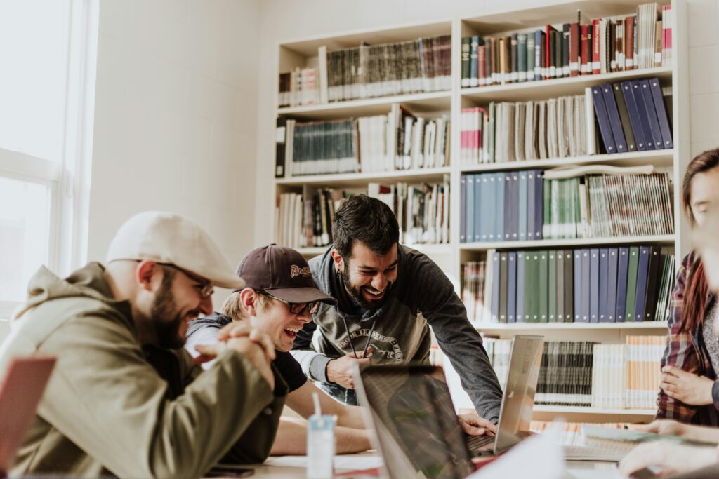 Three male students laughing while looking at the laptop inside the library