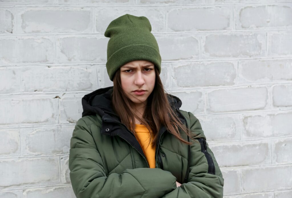 An angry white female student leaning on the class wall with her hands crossed